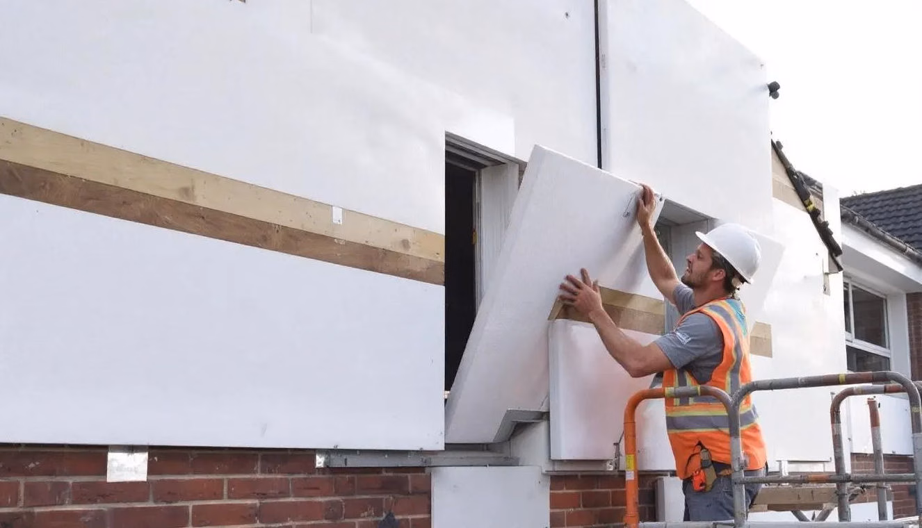 Auf dem Bild sind EPS Dämmplatten aus expandiertem Polystyrol zu sehen, die an einer Hausfassade während der Installation eines Wärmedämmverbundsystems (WDVS) angebracht werden. Die Platten sind leicht und bieten hervorragende Eigenschaften zur Wärmedämmung, während im Hintergrund Bauarbeiten sichtbar sind.