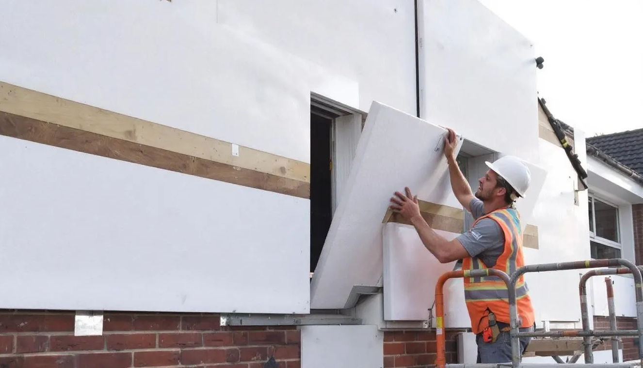 Auf dem Bild sind EPS Dämmplatten aus expandiertem Polystyrol zu sehen, die an einer Hausfassade während der Installation eines Wärmedämmverbundsystems (WDVS) angebracht werden. Die Platten sind leicht und bieten hervorragende Eigenschaften zur Wärmedämmung, während im Hintergrund Bauarbeiten sichtbar sind.